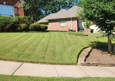 2000x924.jpeg.a9830f6bf6474b8f8b1f85df9e2f808a Well-maintained lawn with striped grass, landscaped shrubs, and a brick house in Central Arkansas, showcasing APEX Lawn Care's professional lawn care services.