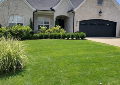 A single-story building with a manicured lawn, beige exterior walls, and a black garage door under a sunny sky. - Little Rock Lawn Care and Mowing Services by Apex Lawn Care Lush green lawn with neatly trimmed grass and ornamental shrubs in front of a modern home, showcasing APEX Lawn Care services in Little Rock, Arkansas.