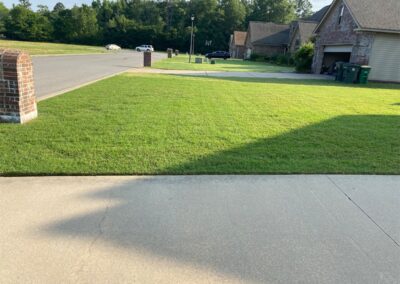 A residential street with a well-manicured lawn and shadow of an employee in the foreground. - Little Rock Lawn Care and Mowing Services by Apex Lawn Care Lush green lawn maintained by APEX Lawn Care in a residential setting, showcasing professional lawn care services in Little Rock, Arkansas.