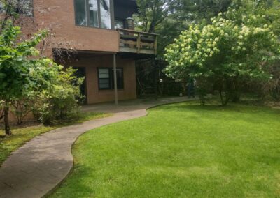 A two-story brick house with a wooden deck and spiral staircase surrounded by greenery. - Little Rock Lawn Care and Mowing Services by Apex Lawn Care Lush green lawn with curved pathway leading to a residential building, showcasing APEX Lawn Care's landscaping services in Little Rock, Arkansas.