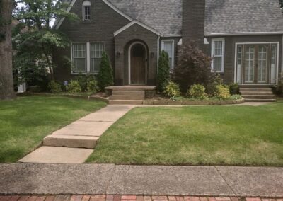 A brick pathway leading to a traditional house with a gabled roof and arched front door with a perfectly manicured lawn. - Little Rock Lawn Care and Mowing Services by Apex Lawn Care Lawn care showcase featuring well-maintained grass and landscaped front yard of a residential property in Little Rock, Arkansas, highlighting APEX Lawn Care services.