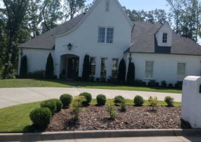 White two-story suburban house with a well-manicured lawn and shrubbery under a clear sky. - Little Rock Lawn Care and Mowing Services by Apex Lawn Care Lawn care services by APEX Lawn Care showcasing a well-manicured residential property with landscaped garden beds and neatly trimmed bushes in Little Rock, Arkansas.
