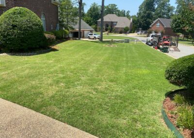 A well-manicured lawn in front of suburban houses on a sunny day with employees working. - Little Rock Lawn Care and Mowing Services by Apex Lawn Care Well-maintained lawn in Little Rock, Arkansas, showcasing lush green grass and landscaped edges, highlighting APEX Lawn Care's professional services.