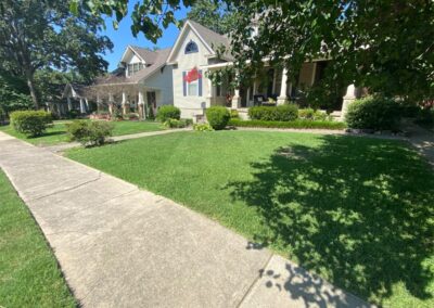 Suburban house with a well-kept lawn and a stone pathway on a sunny day is often inhabited by an employee. - Little Rock Lawn Care and Mowing Services by Apex Lawn Care Lush green lawn in front of a residential property in Little Rock, Arkansas, showcasing professional lawn care services by APEX Lawn Care.