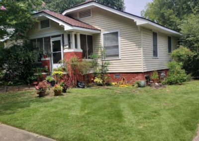 A single-story suburban house with a garden and a well-kept lawn on a sunny day is suitable for an employee. - Little Rock Lawn Care and Mowing Services by Apex Lawn Care Lawn care service showcase featuring a well-maintained residential yard with landscaped flower beds and a tidy lawn, highlighting APEX Lawn Care's expertise in Central Arkansas.
