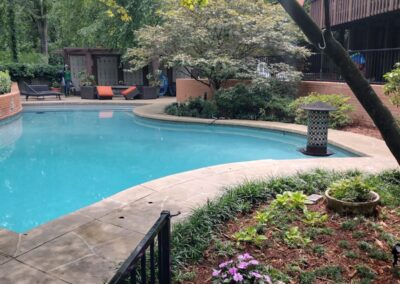 A serene outdoor swimming pool area surrounded by lush greenery and trees, featuring a lounging area and a fence. This space is ideal for anyone seeking relaxation or an outdoor meeting location. - Little Rock Lawn Care and Mowing Services by Apex Lawn Care Lush backyard with a swimming pool, surrounded by landscaped gardens and patio furniture, showcasing APEX Lawn Care's landscaping services in Little Rock, Arkansas.