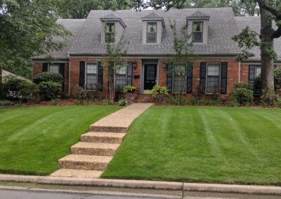 Traditional two-story brick house with manicured lawn and a stone pathway leading to a green front door, suitable for an employee. - Little Rock Lawn Care and Mowing Services by Apex Lawn Care Lush green lawn with neatly trimmed grass and a stone pathway leading to a brick house, showcasing professional lawn care services by APEX Lawn Care in Little Rock, Arkansas.