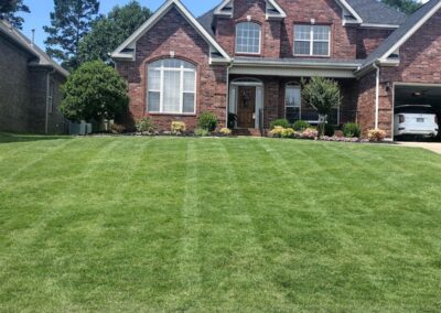 An employee brick suburban house with a well-manicured lawn and a partly open garage under a clear blue sky. - Little Rock Lawn Care and Mowing Services by Apex Lawn Care Well-maintained green lawn in front of a brick house, showcasing APEX Lawn Care services in Little Rock, Arkansas.