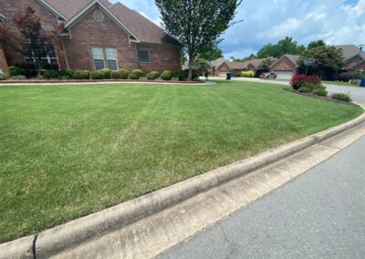 A well-manicured front lawn of a brick house with a curved sidewalk and clear skies. - Little Rock Lawn Care and Mowing Services by Apex Lawn Care Lush green lawn with neatly trimmed grass and well-maintained landscaping in a residential area, showcasing APEX Lawn Care services in Little Rock, Arkansas.