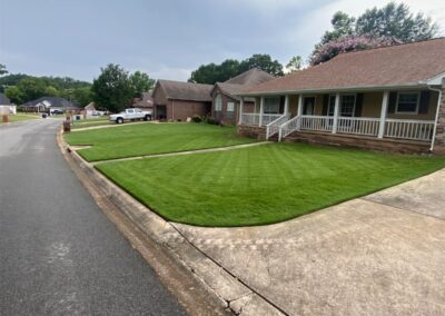 A residential street with well-maintained lawns and single-story houses under a clear sky. - Little Rock Lawn Care and Mowing Services by Apex Lawn Care Lush, manicured lawn in front of a residential home in Little Rock, Arkansas, showcasing APEX Lawn Care's professional lawn care services.
