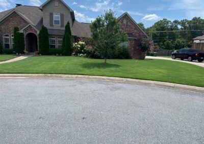 A suburban house with a well-maintained lawn under a clear sky. - Little Rock Lawn Care and Mowing Services by Apex Lawn Care Lawn care service showcasing a well-maintained residential yard in Little Rock, Arkansas, featuring green grass, landscaped flower beds, and a brick house exterior.