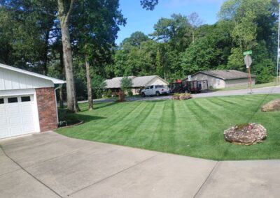 A Little Rock Metro Area scene with well-maintained lawns and driveways in front of single-story homes on a sunny day. - Little Rock Lawn Care and Mowing Services by Apex Lawn Care Well-maintained lawn with striped mowing pattern, residential homes in background, showcasing APEX Lawn Care services in Little Rock, Arkansas.