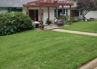 The employee resides in a Little Rock Metro Area Suburban house with a green lawn and a wooden pergola over the front porch. - Little Rock Lawn Care and Mowing Services by Apex Lawn Care Lush green lawn with well-maintained landscaping and a wooden pergola in a residential yard, showcasing APEX Lawn Care's professional lawn care services in Little Rock, Arkansas.