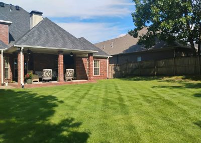 large-10 Well-maintained lawn with striped grass and a brick patio featuring two chairs, showcasing APEX Lawn Care services in Central Arkansas.