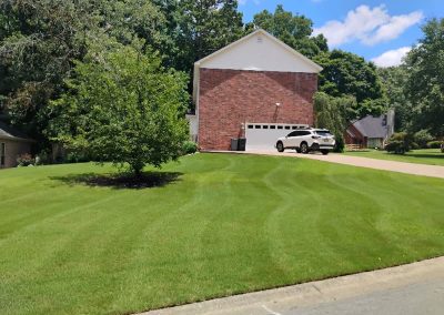 large-19 Well-maintained green lawn with neatly striped grass, featuring a brick house and a parked white SUV in Central Arkansas.