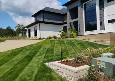 large-2 Lush green lawn with striped mowing patterns, landscaped garden beds, and modern home architecture in Central Arkansas, showcasing APEX Lawn Care's professional lawn care services.