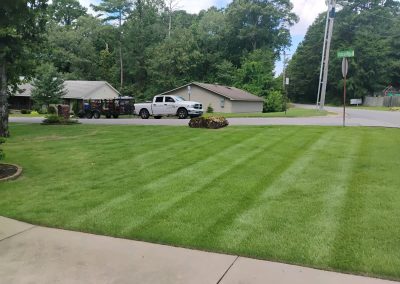 large-20 Well-maintained lawn with striped grass, residential homes in the background, and a service truck parked nearby, showcasing APEX Lawn Care's professional lawn care services in Central Arkansas.
